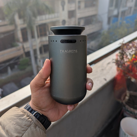 Person holding a gray metallic car diffuser machine called 'Blujay' from the brand 'Fragrens'.